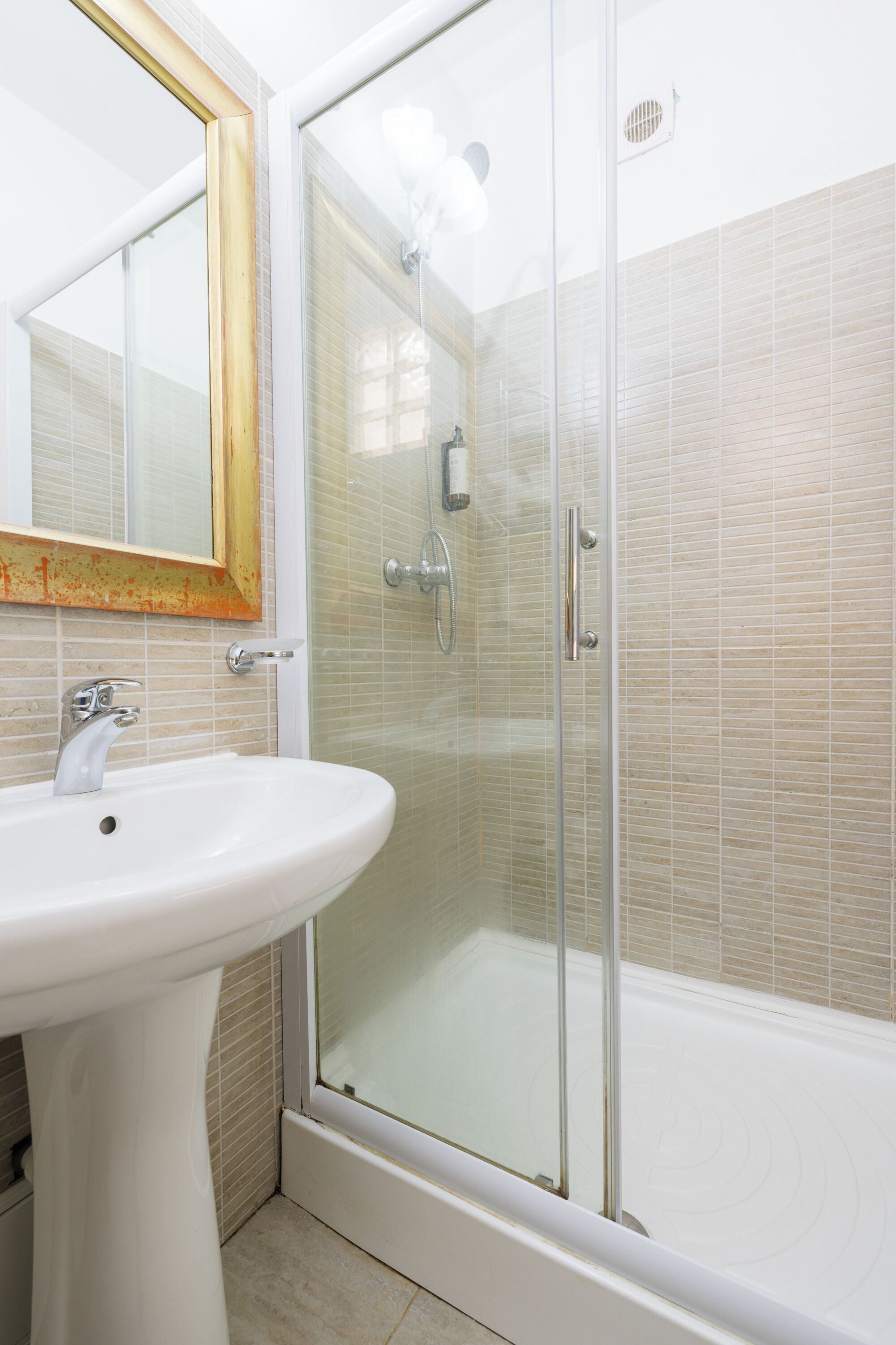 A bathroom with a glass shower enclosure, a white sink, and a mirror with a wooden frame.