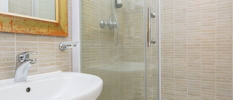 A bathroom with a glass shower enclosure, a white sink, and a mirror with a wooden frame.