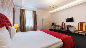 A hotel room with a large bed, a desk with a chair, a television, and a wardrobe.