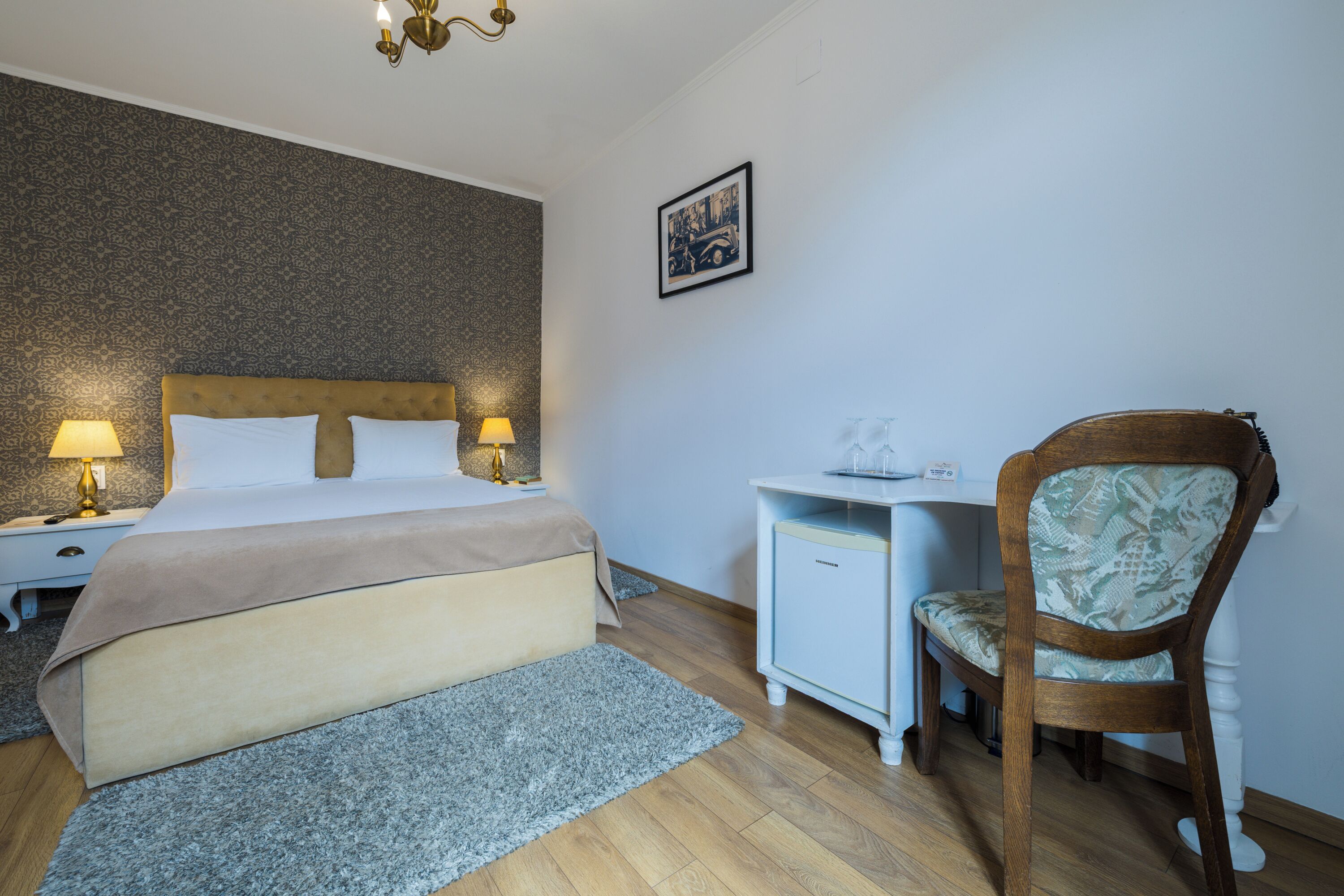 A bedroom with a bed, bedside tables, a desk, a chair, and a wall-mounted picture.