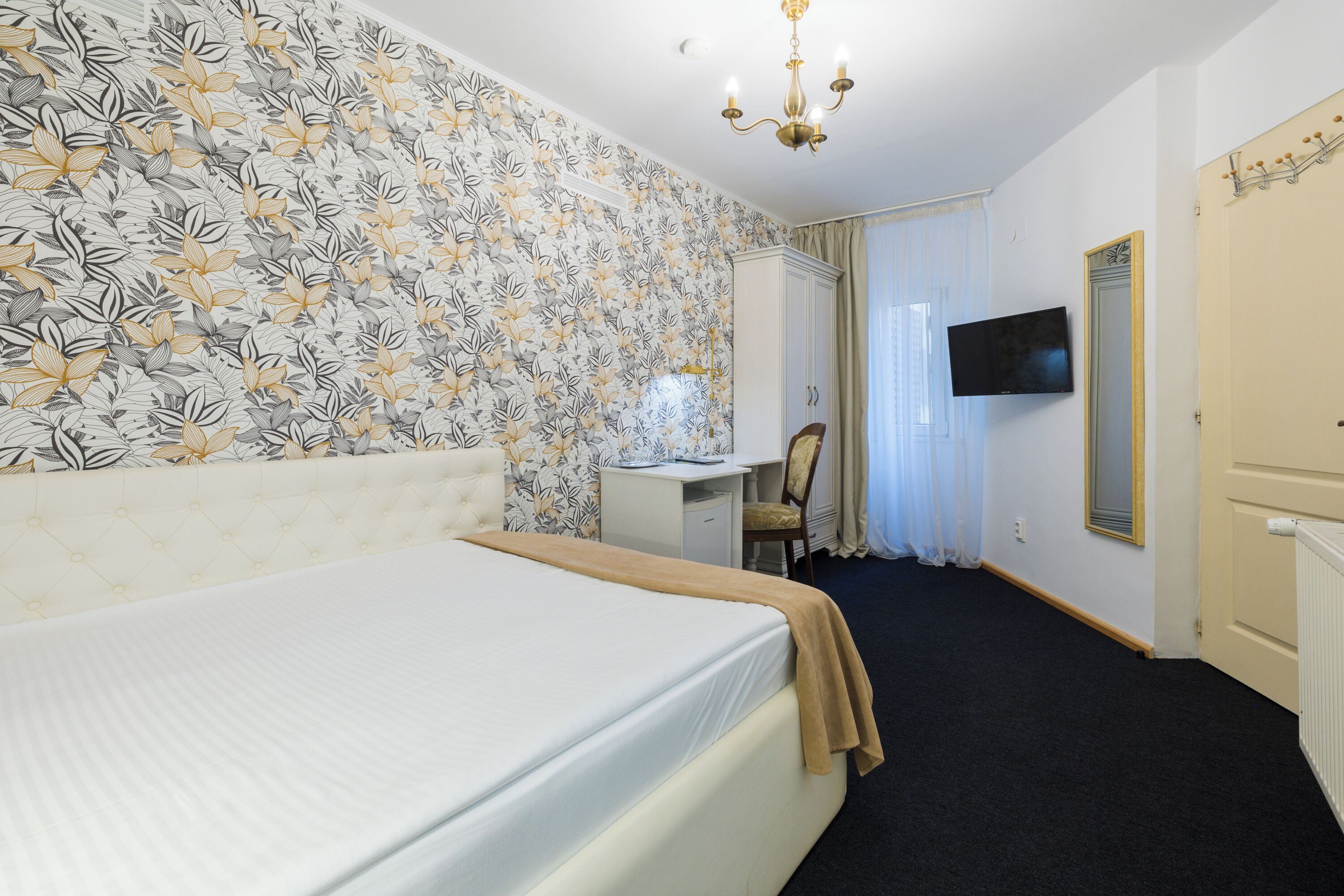 A hotel room with a bed, a desk, a chair, a television, and a wardrobe.