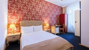 A hotel room with a large bed, two bedside tables with lamps, a desk, a chair, and a wardrobe.