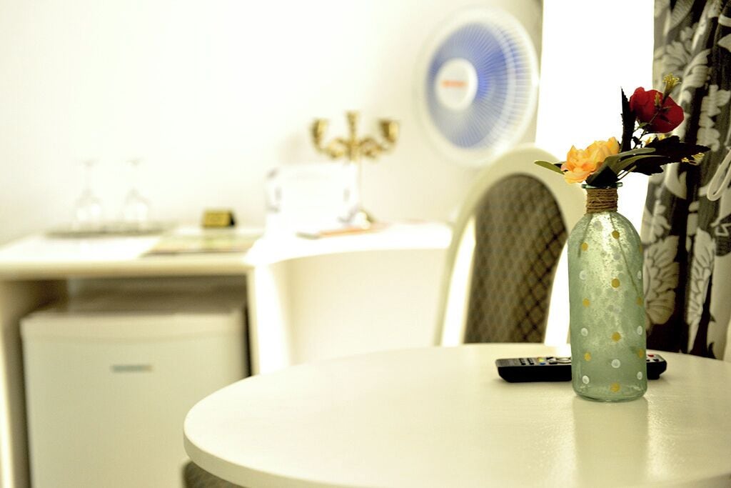 A round table with a vase of flowers, a remote control, and a fan in the background.