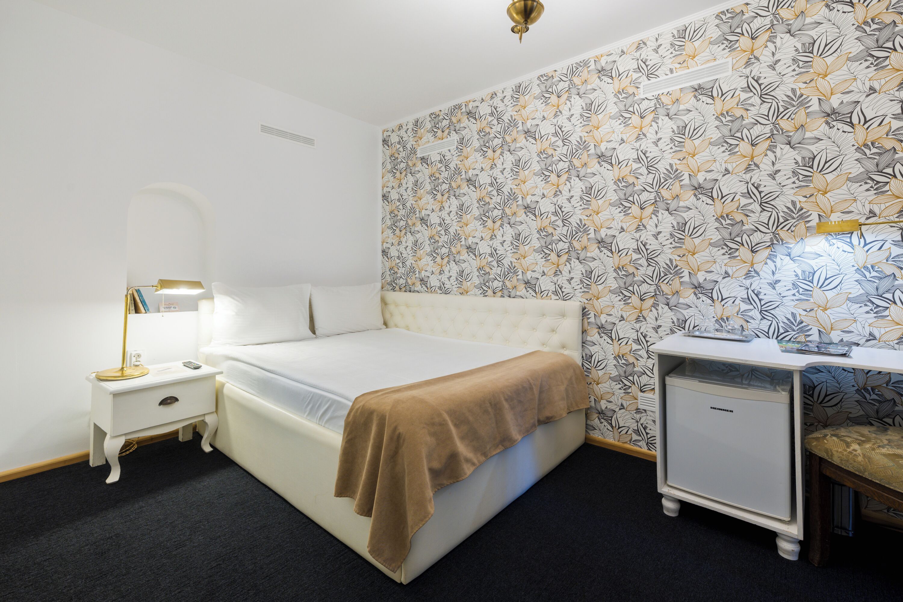 A neatly arranged bedroom with a bed, bedside table, lamp, and a small cabinet.
