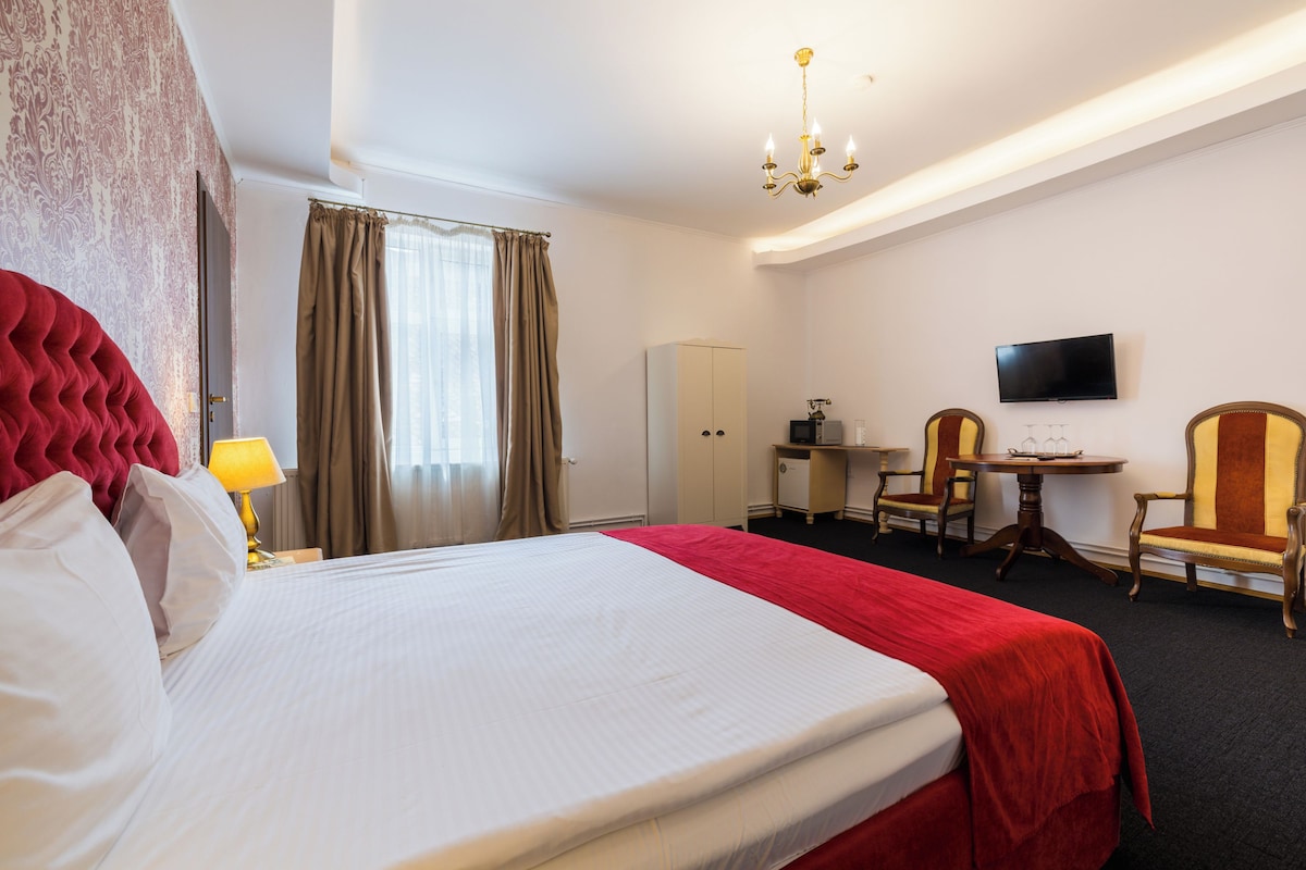 A hotel room with a large bed, a desk with a chair, a television, and a wardrobe.