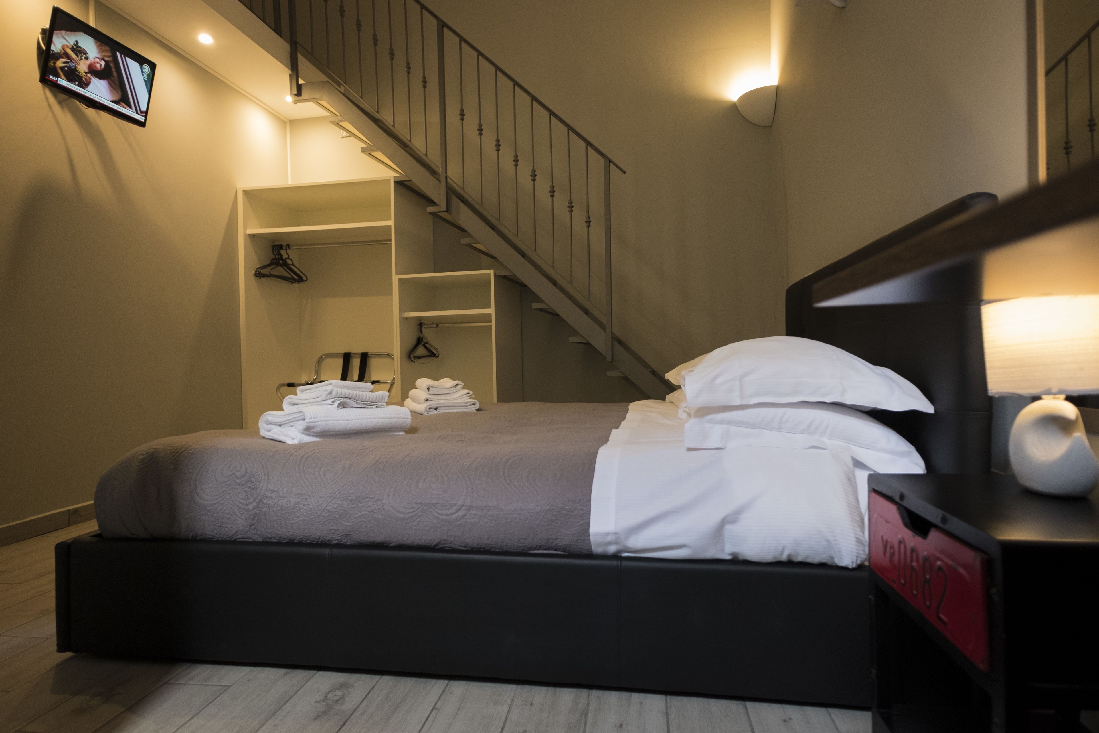 A modern hotel room with a large bed, a wooden staircase, and a TV mounted on the wall.