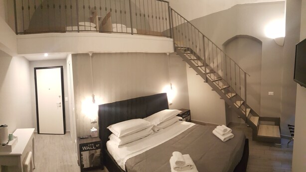 A bedroom with a bed, bedside table, lamp, and a staircase leading to an upper level. - Relais Virginia Home (Sanremo)