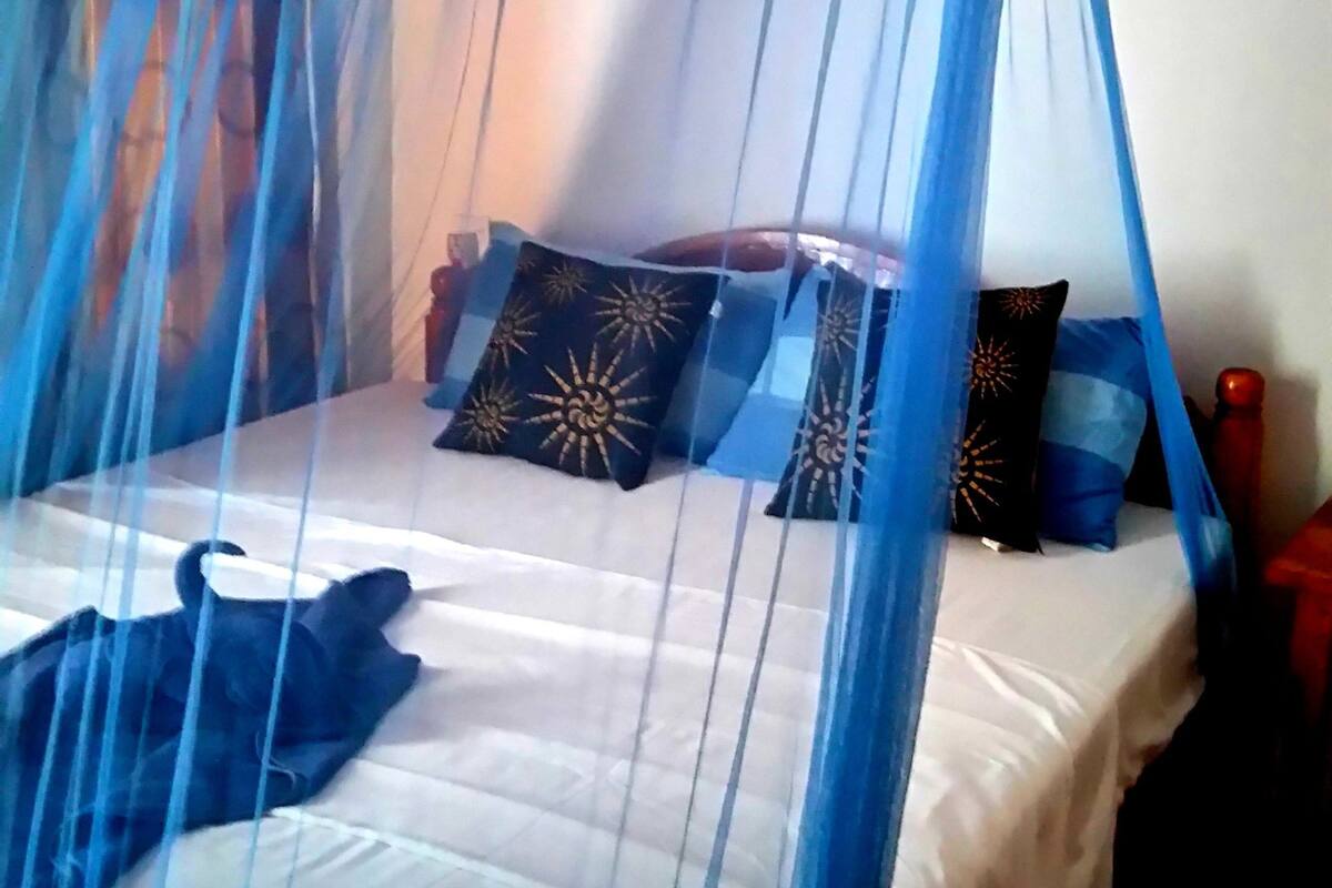 Una cama con dosel, almohadas con motivos de sol y una lámpara fijada a la pared.