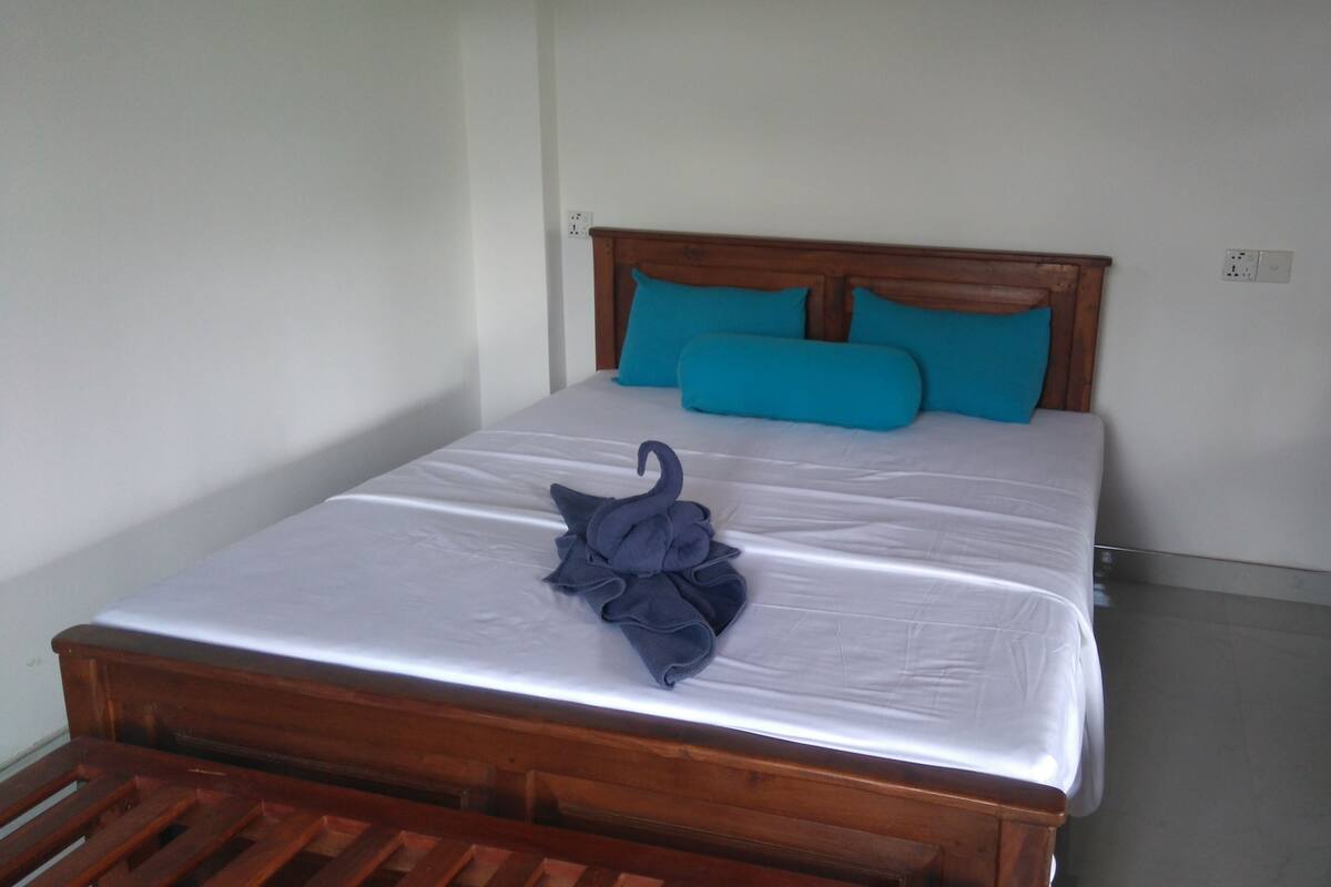 Una cama individual con estructura de madera, ropa de cama blanca y dos almohadas color turquesa.