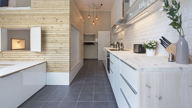 Una cocina moderna con detalles de madera, un horno empotrado y una encimera con una cafetera y un jarrón de flores.