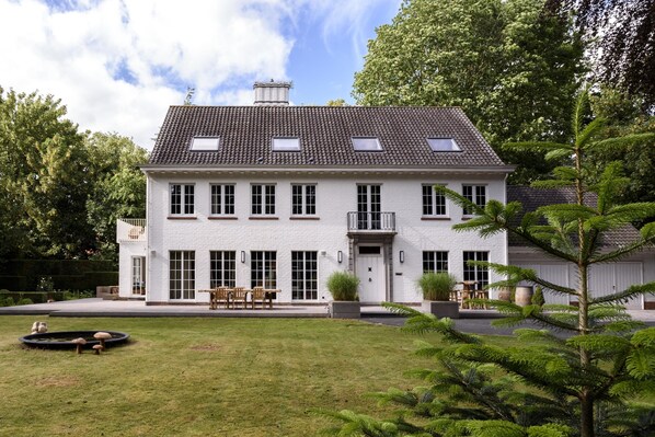 A two-story white house with a tiled roof, multiple windows, and a front porch with outdoor furniture. - B&B Hof Ter Beuke (Bruges)