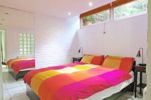 Een kamer met twee bedden, witte bakstenen muren en een raam met uitzicht op groen.