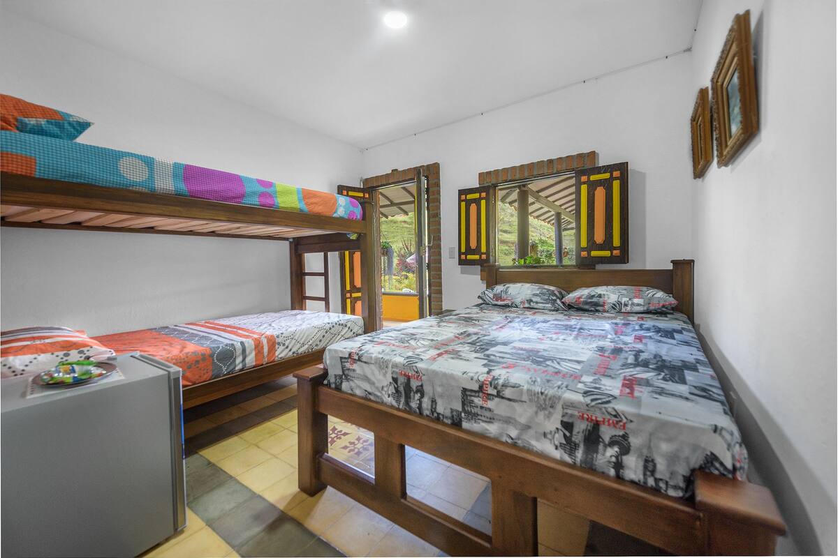 A room with two bunk beds, a small desk, and a window with shutters.