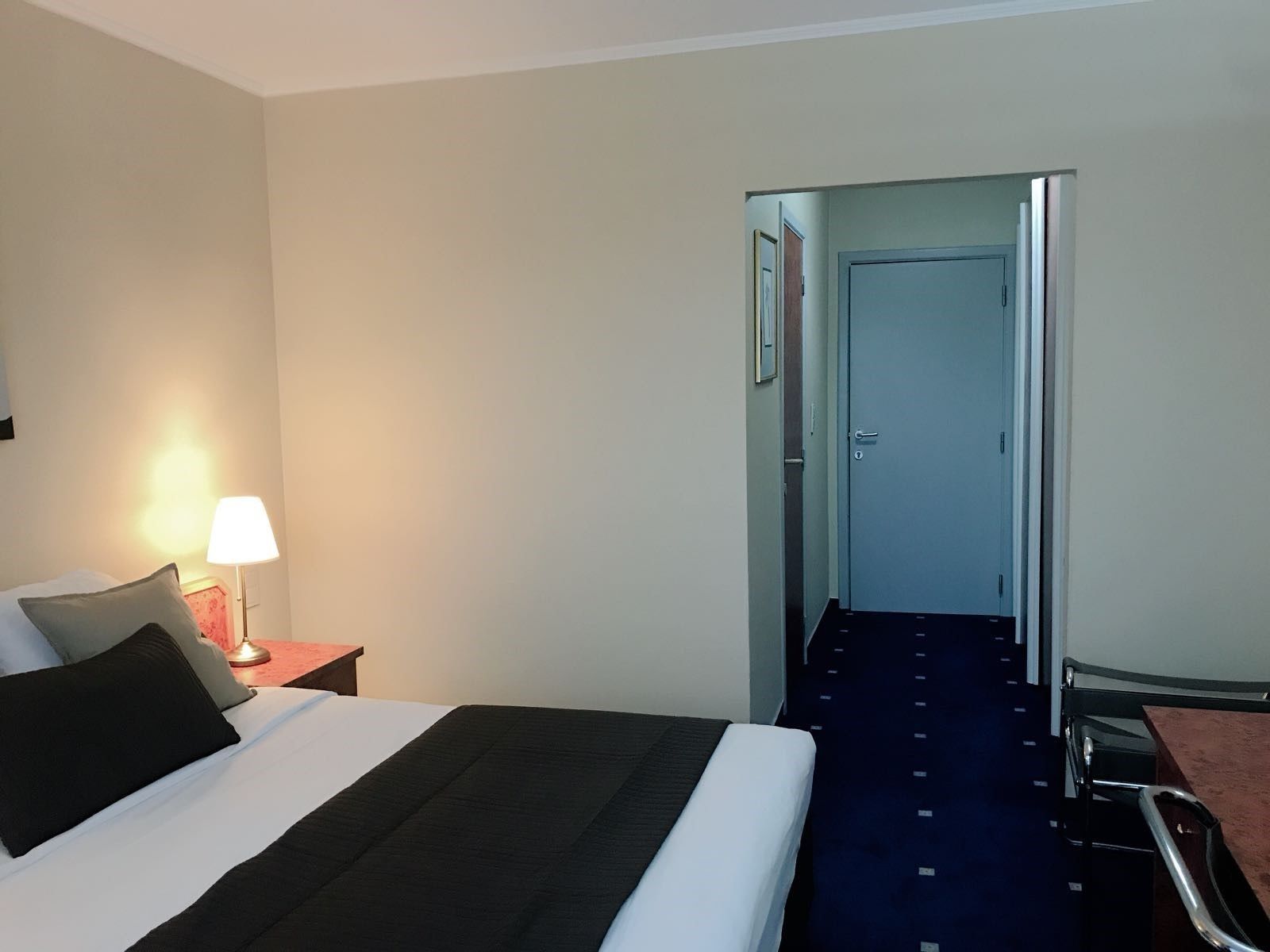 Een hotelkamer met een bed, nachtkastje met lamp, bureau en stoel.