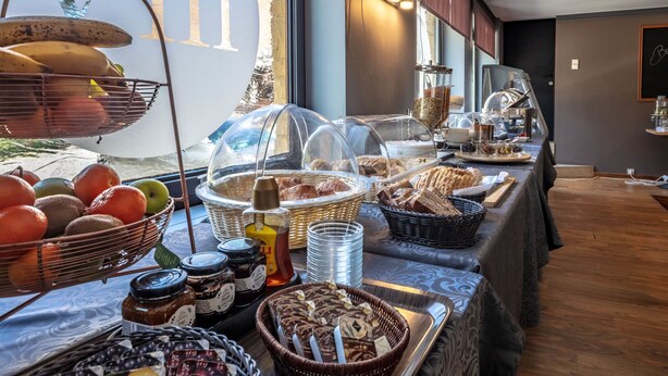 Ein reichhaltiges Buffet mit verschiedenen Speisen und Beilagen, darunter Früchte, Gebäck und Brot, in einem hell erleuchteten Raum mit großen Fenstern.