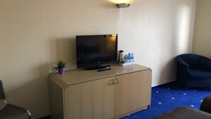 Ein Hotelzimmer mit Fernseher auf einer Holzkabine, einer kleinen Pflanze, einer Wasserflasche und einem blauen Stuhl.