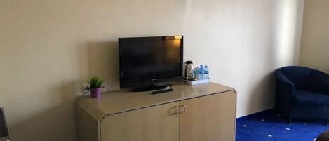 A hotel room with a TV on a wooden cabinet, a small plant, a water bottle, and a blue chair.