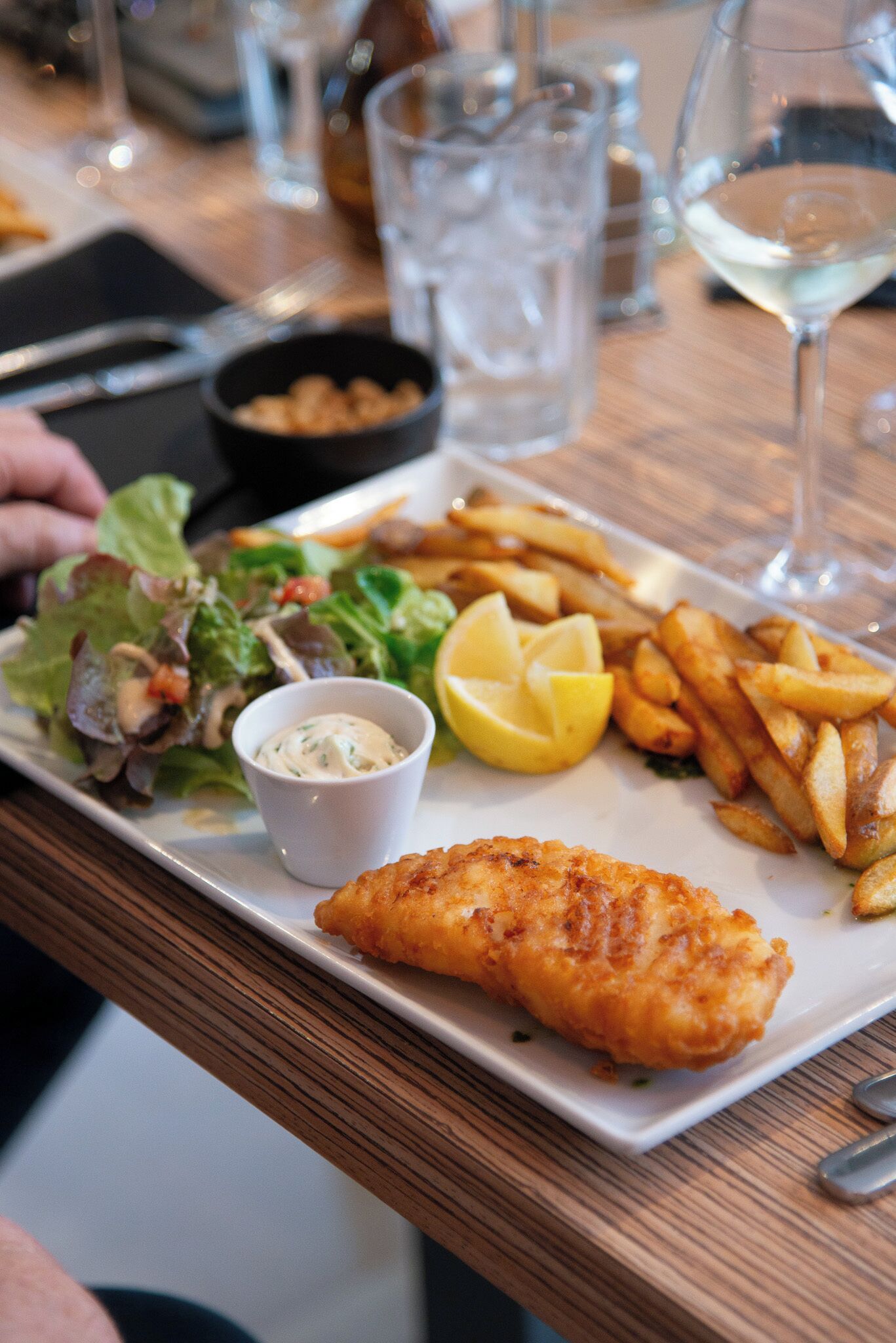 Une assiette contenant un filet de poisson, des frites, une salade et un quartier de citron.
