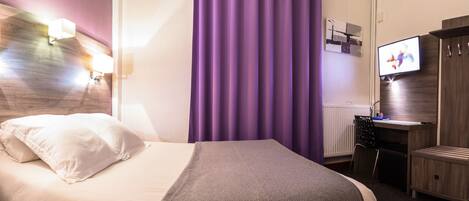 Una habitación de hotel con cama, escritorio, televisor y baño.