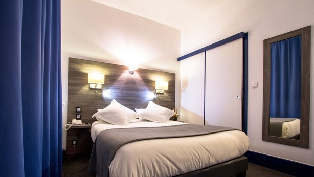 A hotel room with a bed, nightstand, lamp, and a mirror. - Hotel Actuel Chambéry Centre (Chambery)