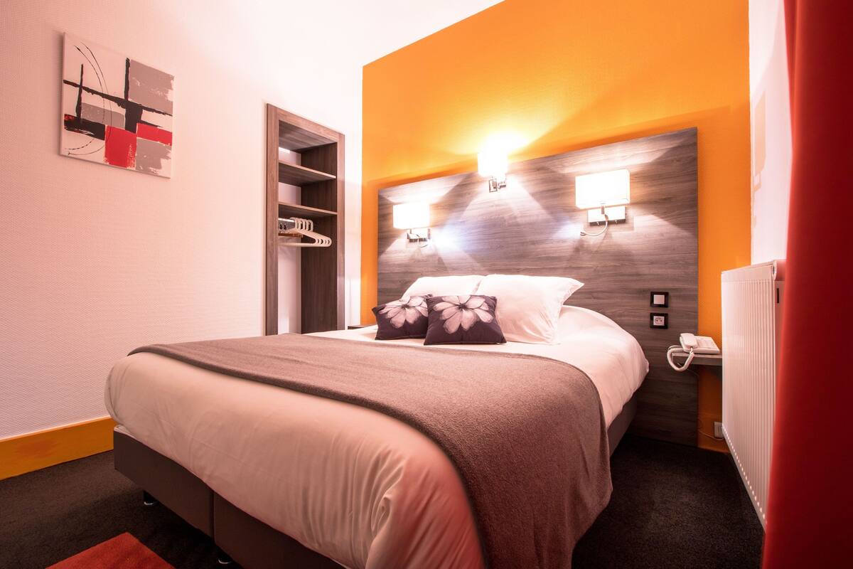 Quarto de hotel com cama, mesa de cabeceira, telefone e luminária na parede.