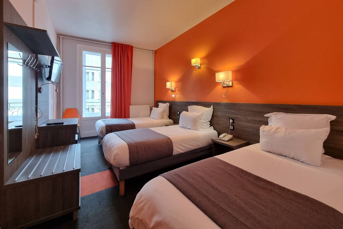 Quarto de hotel com duas camas, uma escrivaninha, uma televisão e uma janela com cortinas.