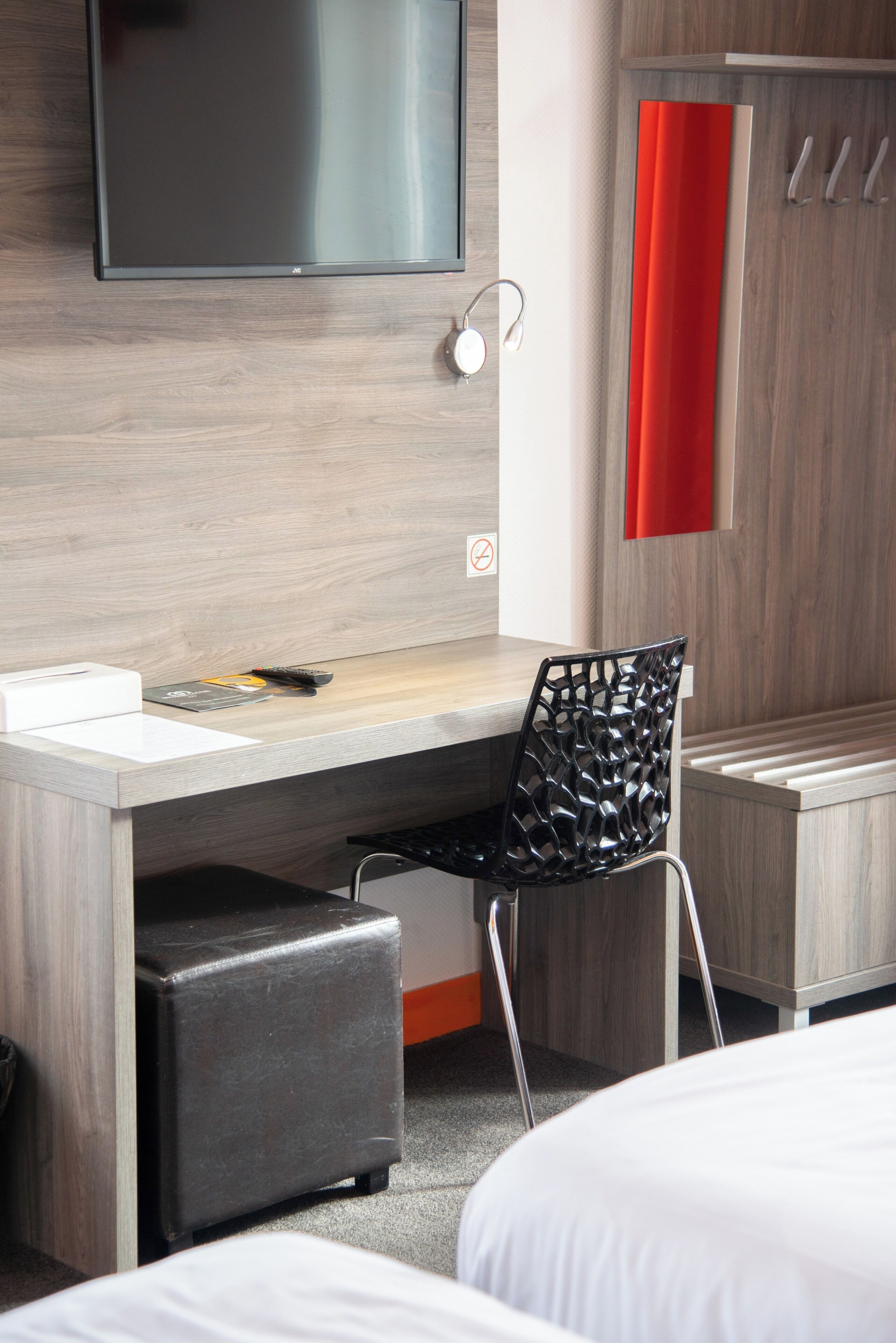 A hotel room with a bed, a desk with a chair, a TV mounted on the wall, and a wardrobe.