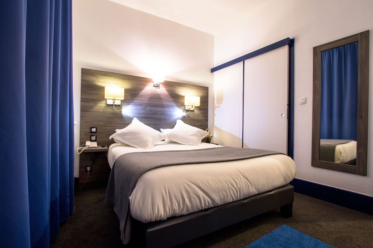Quarto de hotel com cama, mesa de cabeceira, abajur e espelho.