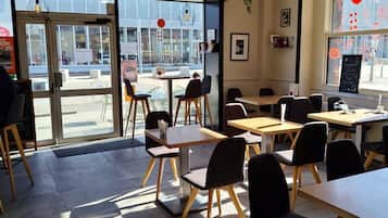 Ein modernes Café mit einer Mischung aus Holz- und schwarzen Stühlen, großen Fenstern und hängenden Pendelleuchten.