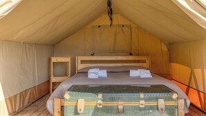 A tent with a single bed, a wooden nightstand, and a green suitcase. - Masseria Prisuti (Manduria)