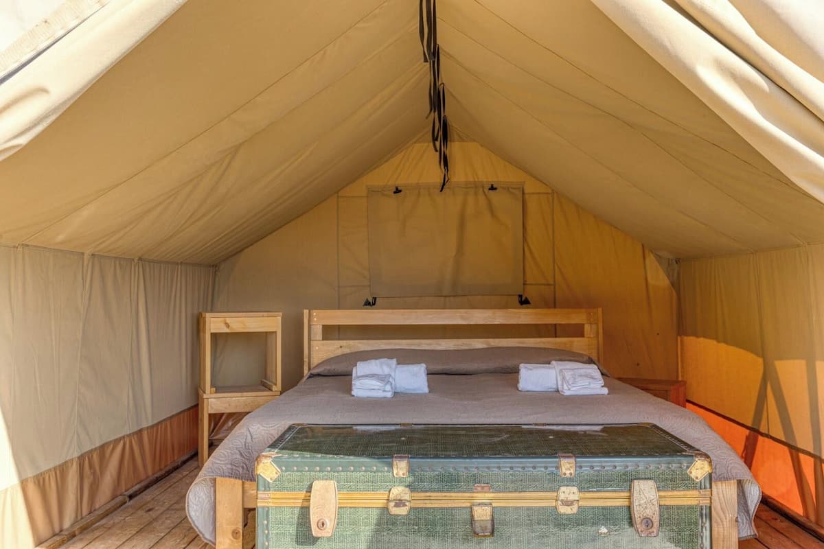 A tent with a single bed, a wooden nightstand, and a green suitcase.