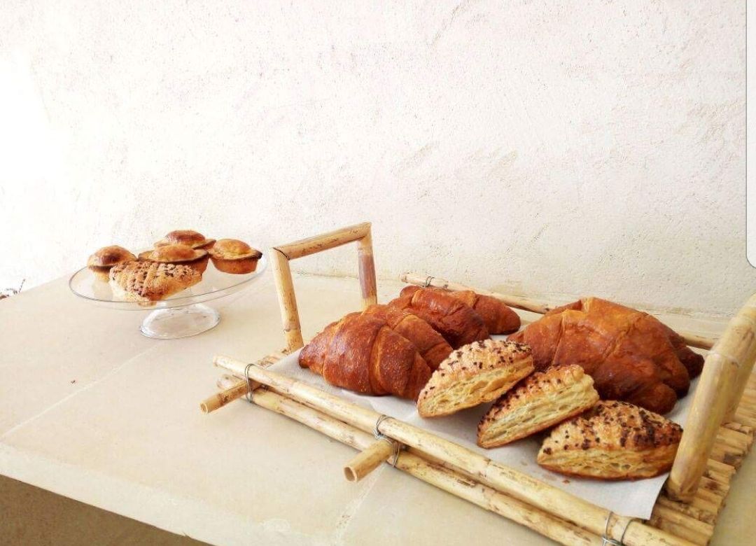 A table with various baked goods, including croissants and muffins, arranged on a bamboo mat.