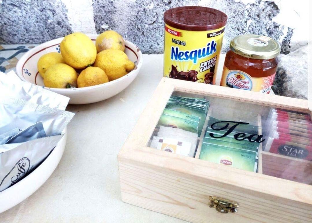 Eine Holzkiste mit Teebeuteln, ein Glas Nesquik Schokolade, ein Honigglas und eine Schüssel Zitronen.