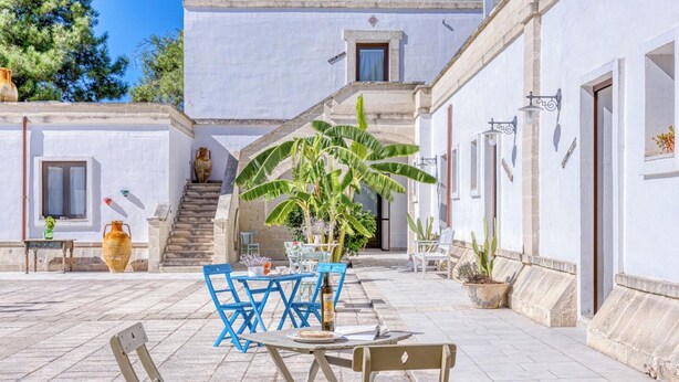 A courtyard with a table and chairs, a staircase, and a building with white walls and a tiled floor. - Masseria Prisuti (Manduria)