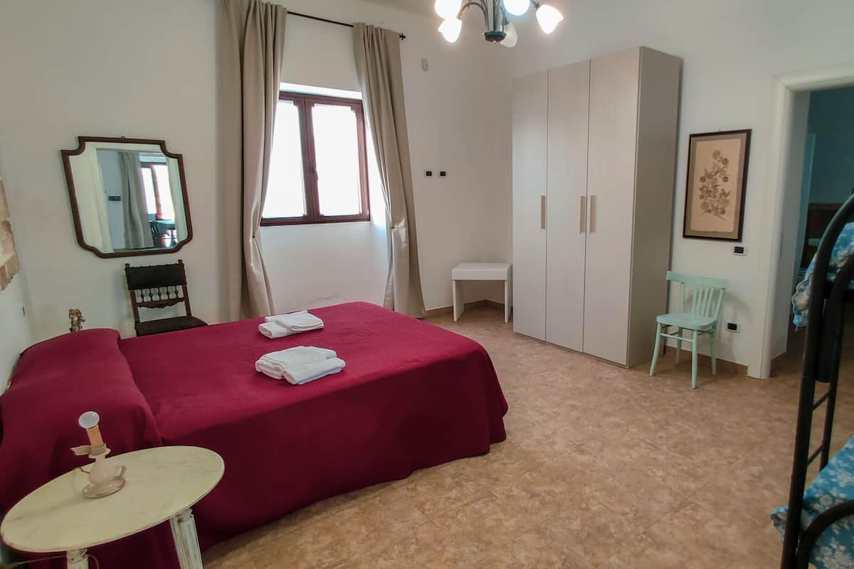 A bedroom with a bed, a small table, a chair, a wardrobe, a mirror, and a bunk bed.