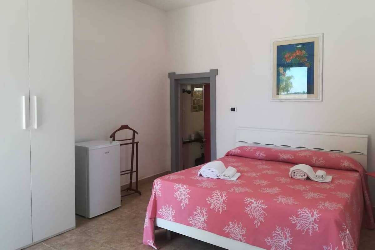 A bedroom with a bed, a wardrobe, a small desk, and a door leading to another room.