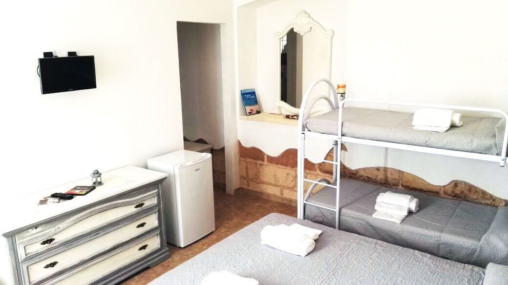 Ein kleines Hotelzimmer mit Etagenbett, einem Schreibtisch mit Stuhl, einem Kühlschrank und einem Wand-Fernseher.