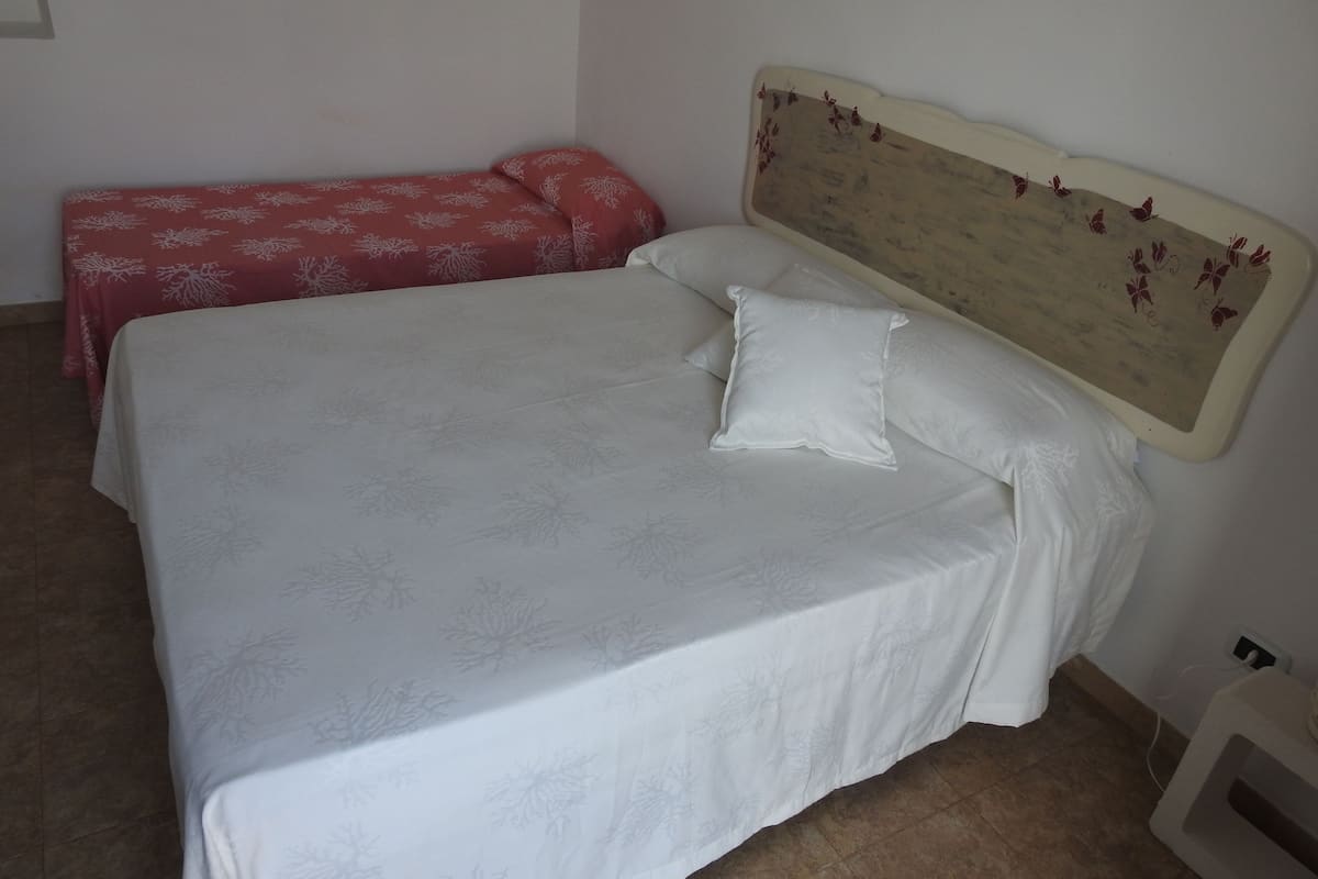 A bed with a white bedspread and two pillows, a red patterned blanket, and a wooden headboard with butterfly designs.