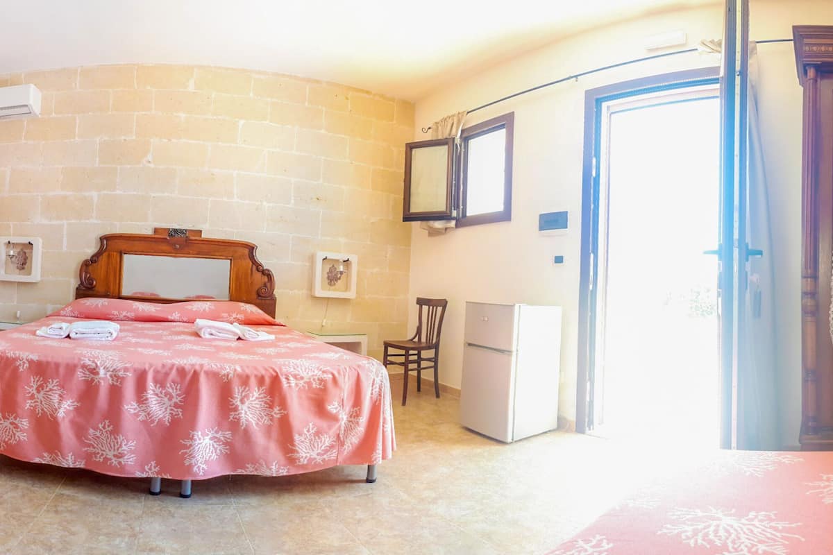 A bedroom with a bed, a chair, a desk, a mirror, a wardrobe, and a door.