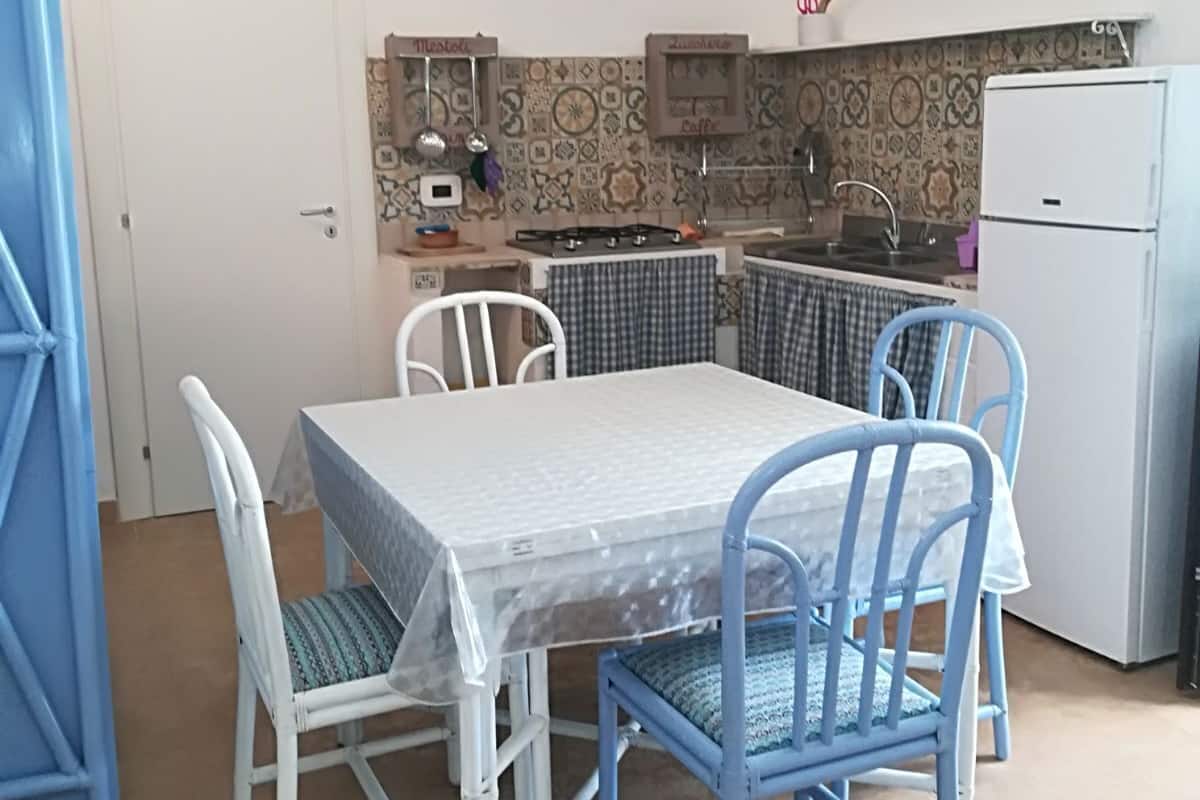 A compact kitchen with a dining table and chairs, a refrigerator, and a tiled backsplash.