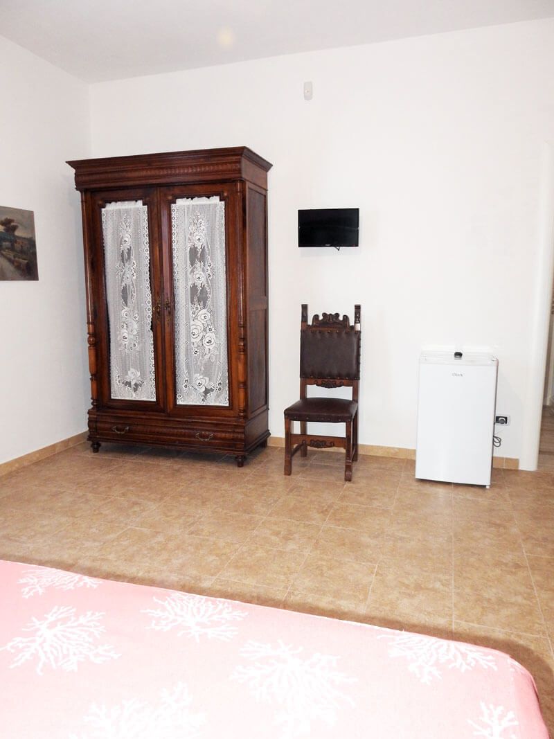A room with a wooden cabinet, a chair, a television mounted on the wall, and a white refrigerator.