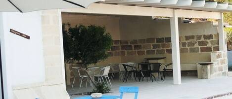 Un'area patio all'aperto con tavoli e sedie, un pergolato e un muro in pietra.