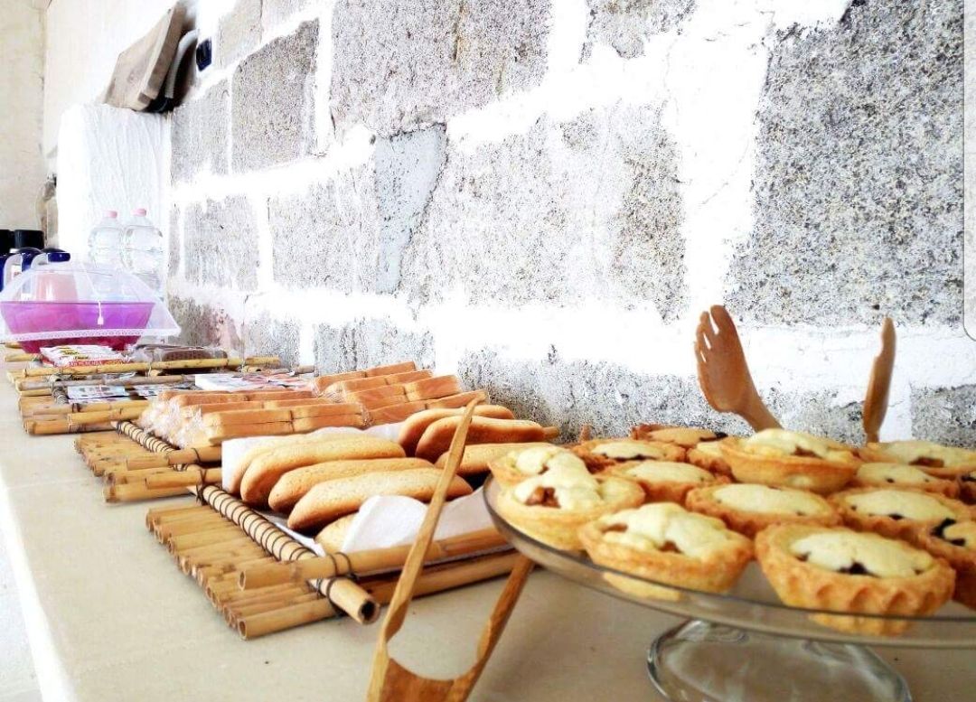 Una mesa de buffet con diversos productos de panadería, incluyendo pan y tartas, frente a una pared de piedra.