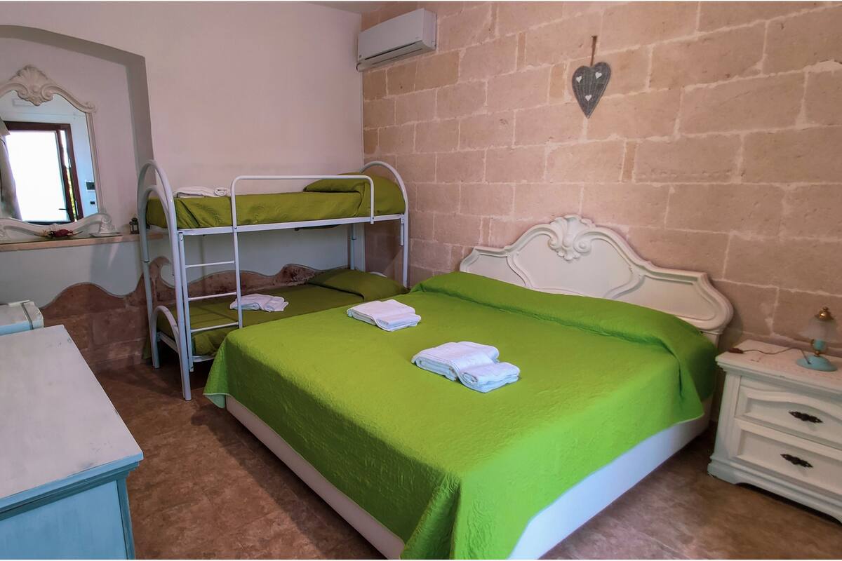 A room with bunk beds, a desk, a mirror, and a bedside table with a lamp.