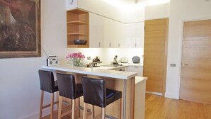 A compact kitchen with a central island, bar stools, a radio, and a painting on the wall. - The London Agent Clerkenwell Super Nice (London)