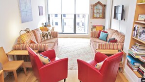 A living room with striped sofas, a red armchair, a wooden table, and a bookshelf. - The London Agent Clerkenwell Super Nice (London)