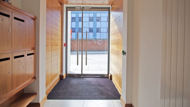 A modern hallway with a wooden bench, a glass door leading outside, and a view of a brick building. - The London Agent Clerkenwell Super Nice (London)