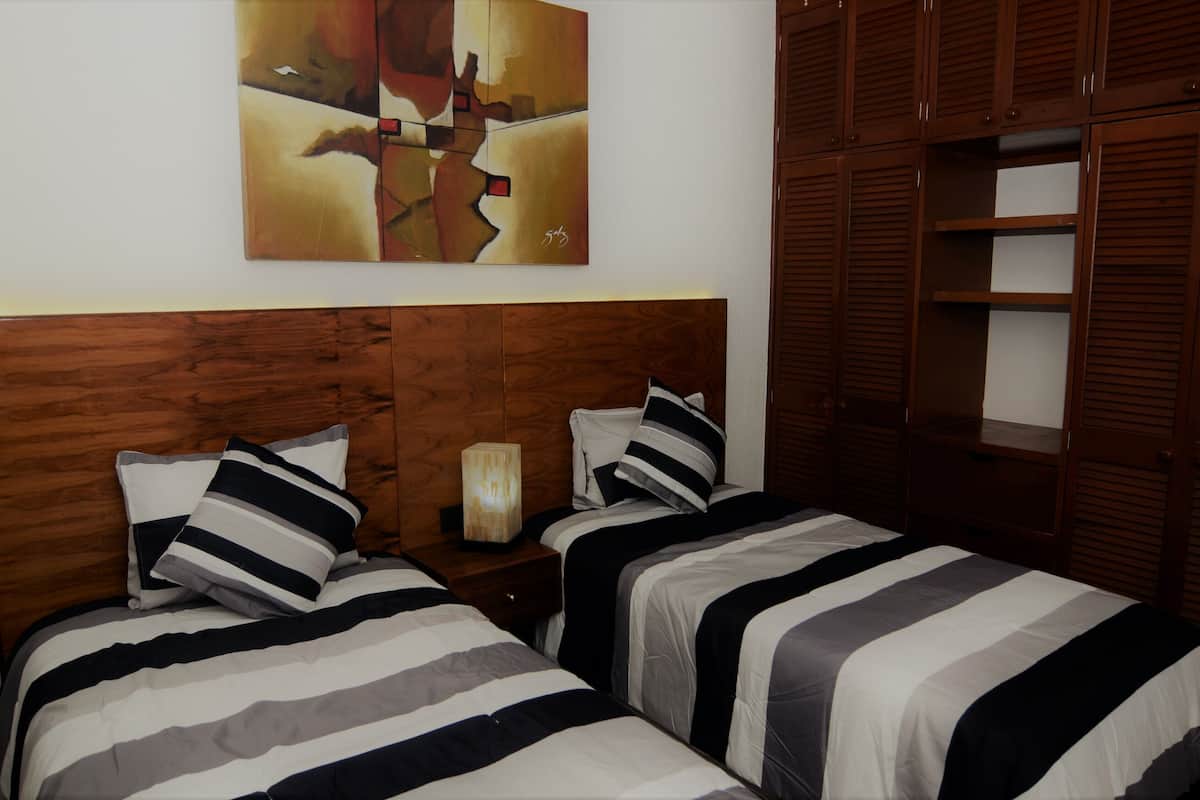 A room with two beds, wooden headboard, a painting on the wall, and a wardrobe with sliding doors.