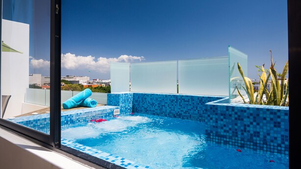 A rooftop pool with blue mosaic tiles, a glass partition, and a view of the cityscape. - Carmen Sol Rentals Apartamentos (Playa del Carmen)