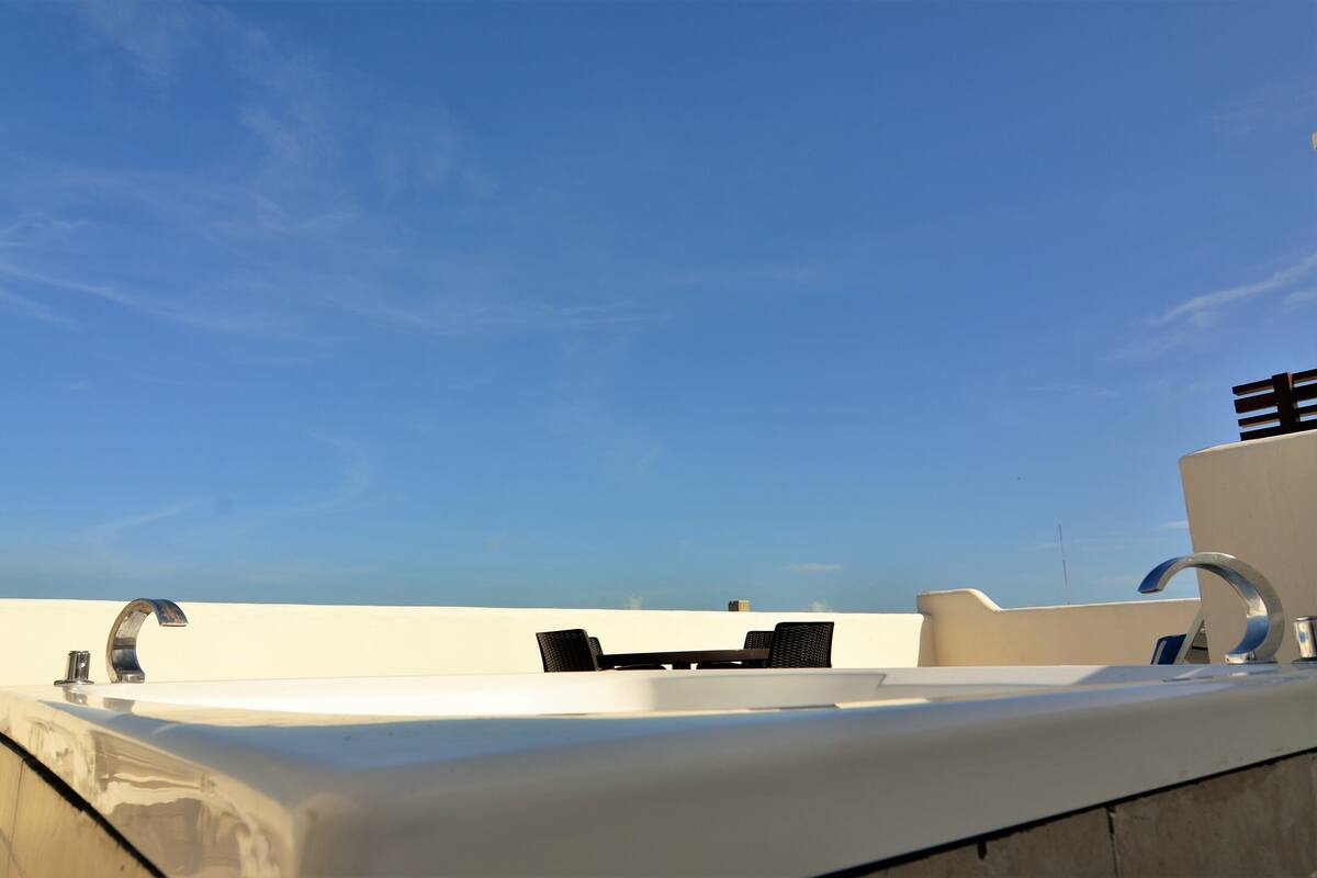 A rooftop terrace with a white sink, two black chairs, and a clear blue sky.